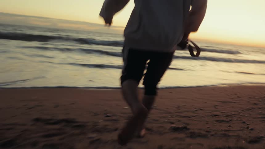 The man is running on the beach while holding a camera
