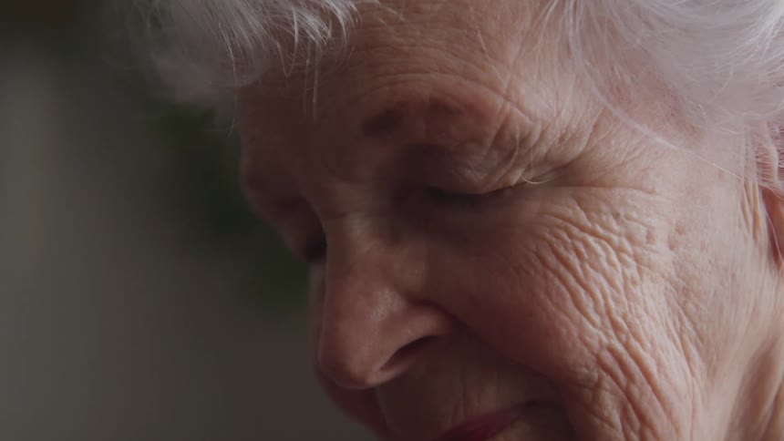 An elderly woman is resting with her eyes closed
