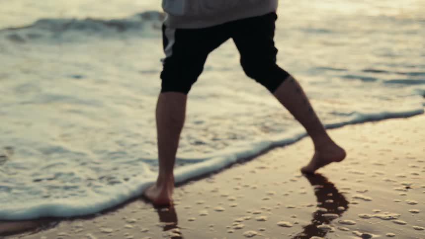 Man walking on the shoreline as the tide rolls in at sunrise
