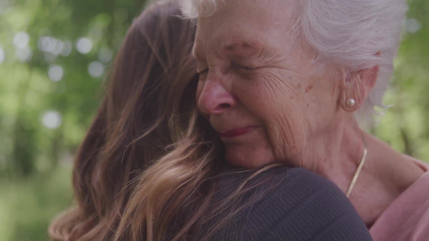 Grandmother hugging her granddaughter outdoors in forest area
