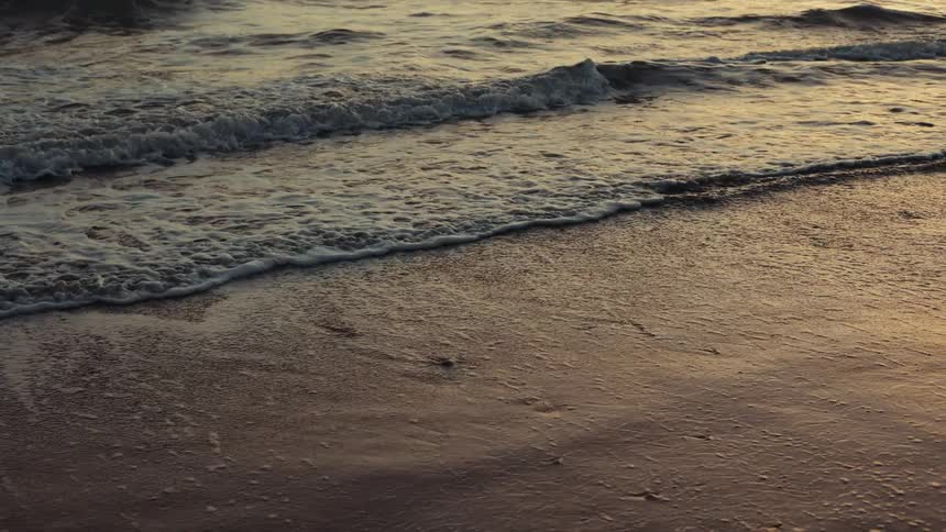 A body of water with rolling waves crashing onto the beach at sunset
