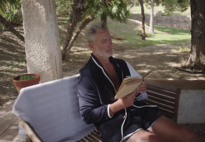 A man is relaxing and reading in his yard
