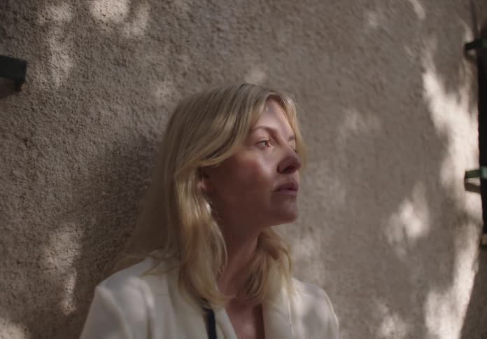 Blonde woman leaning against a wall looking to the side