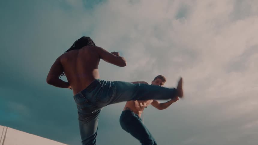 Two shirtless men wearing only pants practicing capoeira