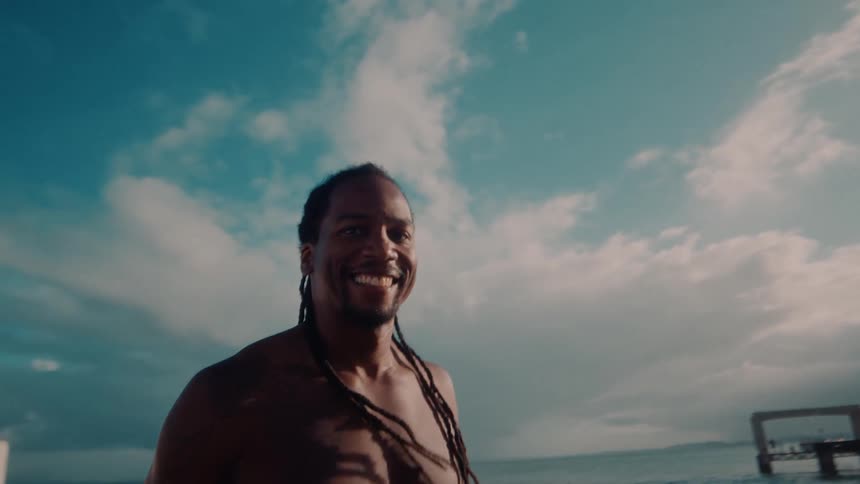 A man smiling clapping his hands and making the hang loose sign with his hands at the beach shore