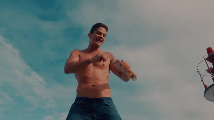 A young man holds and dances with a tambourine beside a lighthouse