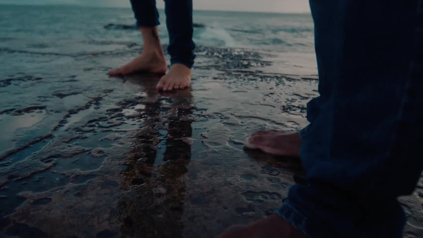 A couple people stand on a rocky coastline