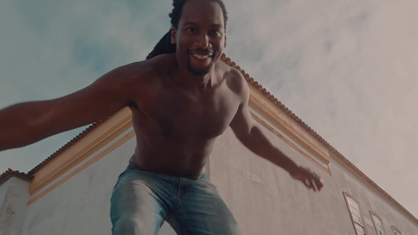 A young man shirtless and wearing jeans dances in the street around midday