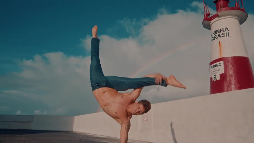 A man performs acrobatics beside a lighthouse around midday