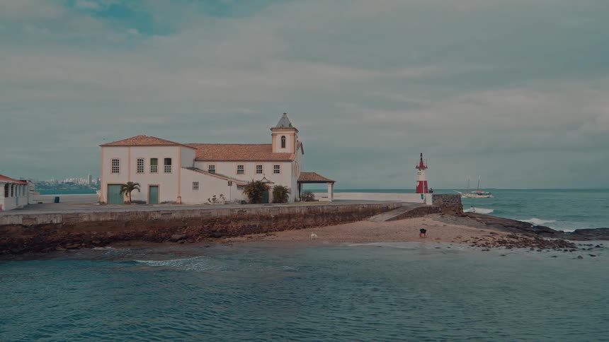 A coastal church stands peacefully by the sea with a lighthouse nearby