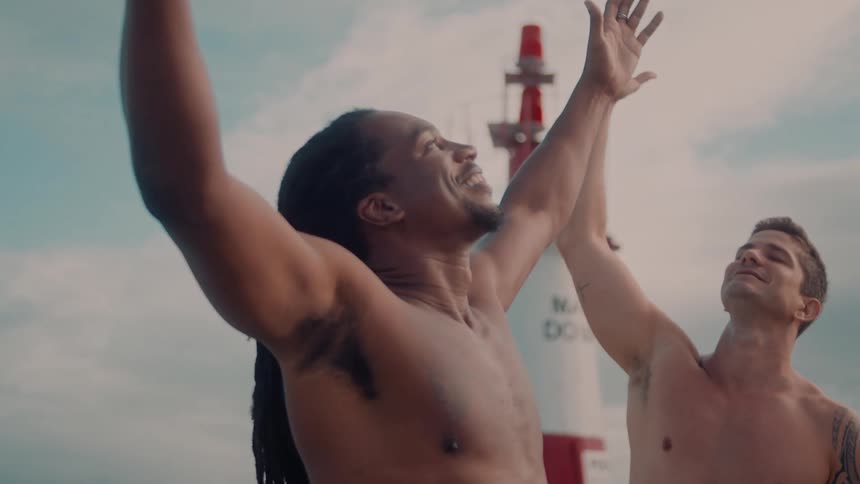 Two men standing on a beach lifting their arms up as they smile at the sun