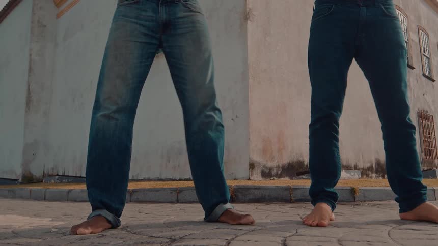 Two men dance barefoot on the side of the road around midday