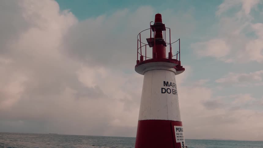 Top of a beacon stands on the coast under a cloudy sky