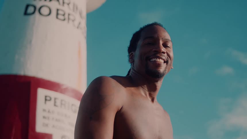 Shirtless man sitting outdoors playing tambourine