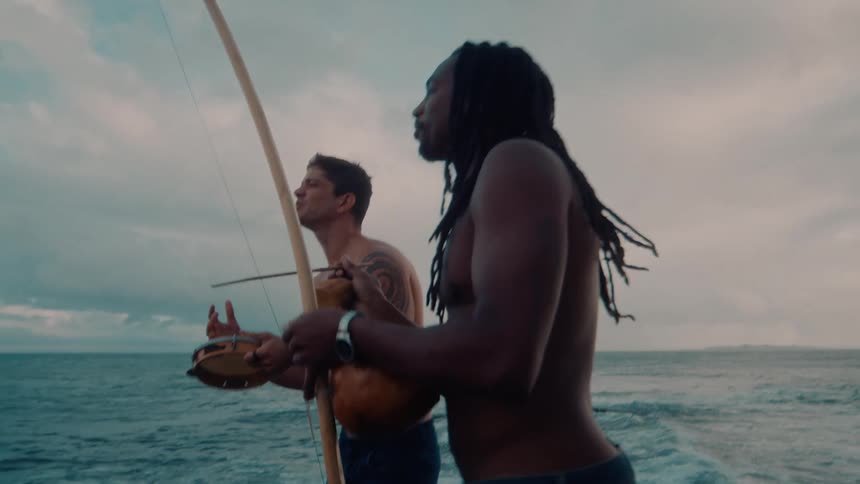Two men play musical instruments and sing on the beach