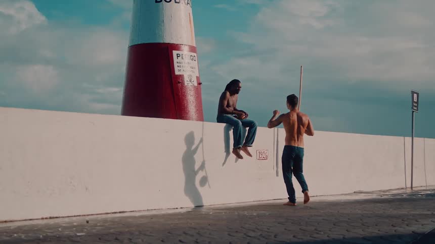 Man greeting another man at a lighthouse with a berimbau