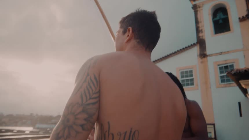 Two shirtless men outdoors playing capoeira berimbau