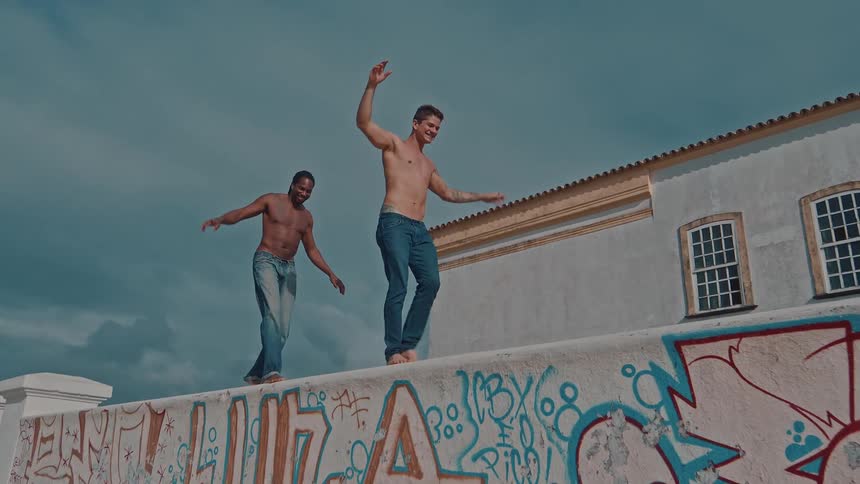 Two shirtless men balance on a graffiticovered wall near a traditional building