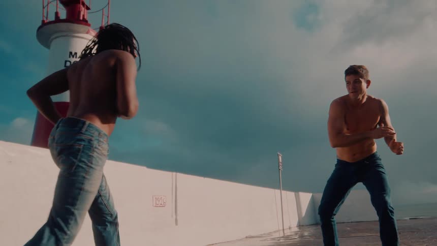Two men perform a dance fight just beside a lighthouse around midday