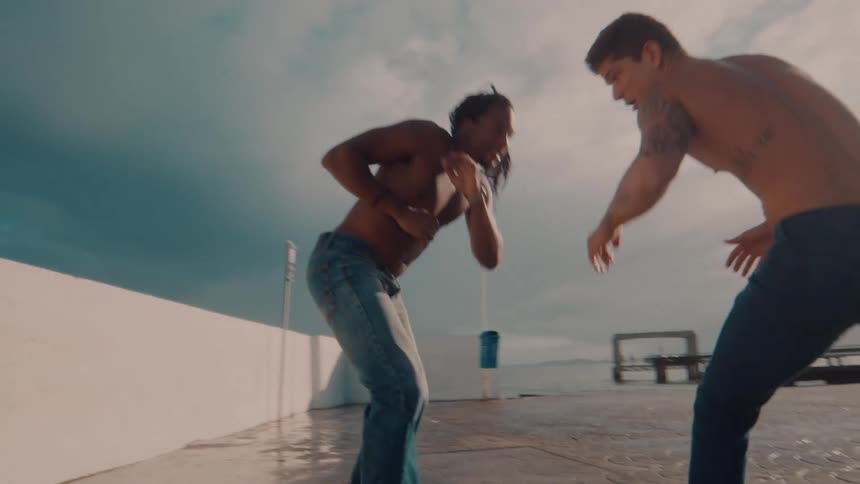 Two people without shirts and wearing jeans in an outdoor capoeira performance
