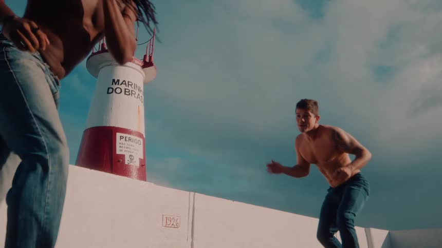 Two shirtless men outdoors fighting capoeira