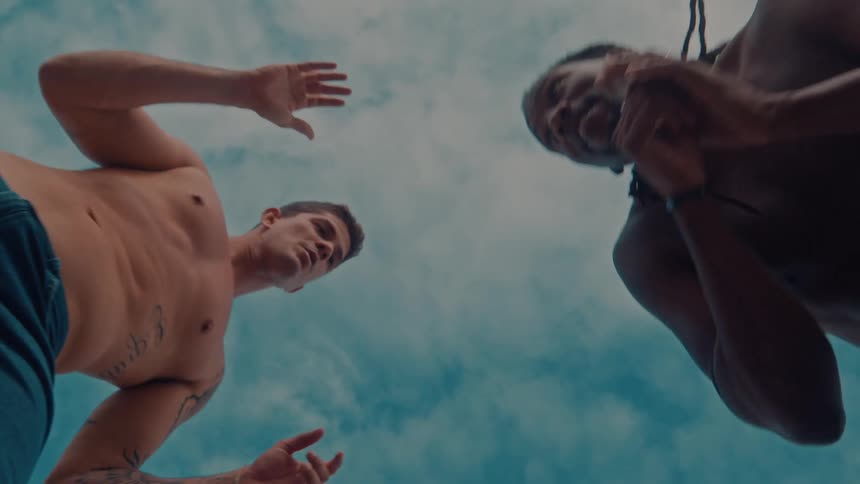 Two men perform capoeira under a cloudy sky viewed from a low angle as they look down toward the camera