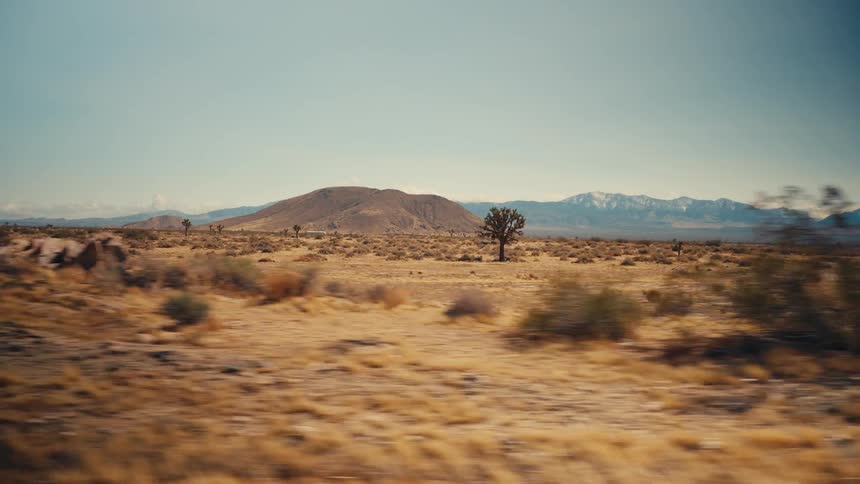 Car drives through desert with dry land and distant hills