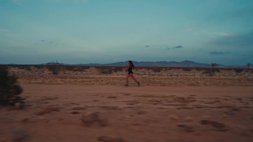 Woman runs along a dirt road passing through the desert after dusk