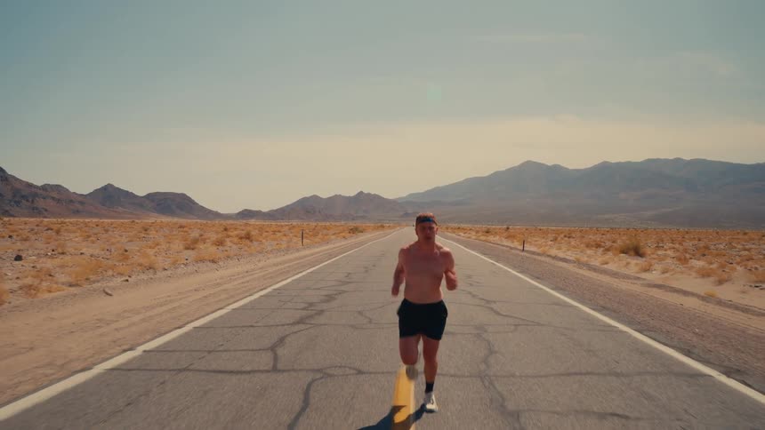 Young man jogs on a road in the middle of a grassland during daytime