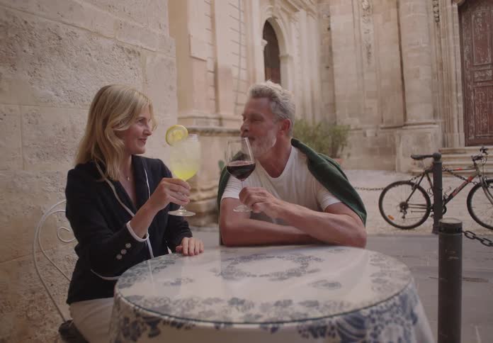 A couple toasts drinks while chatting at an outdoor cafe in a historic setting