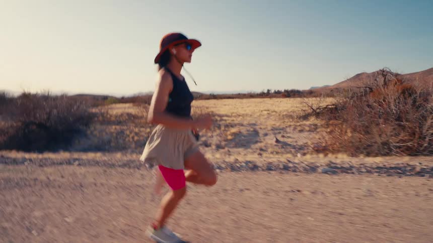 A man running shakes hands with a woman beside the road as she starts running under the sun wearing a hat and earbuds