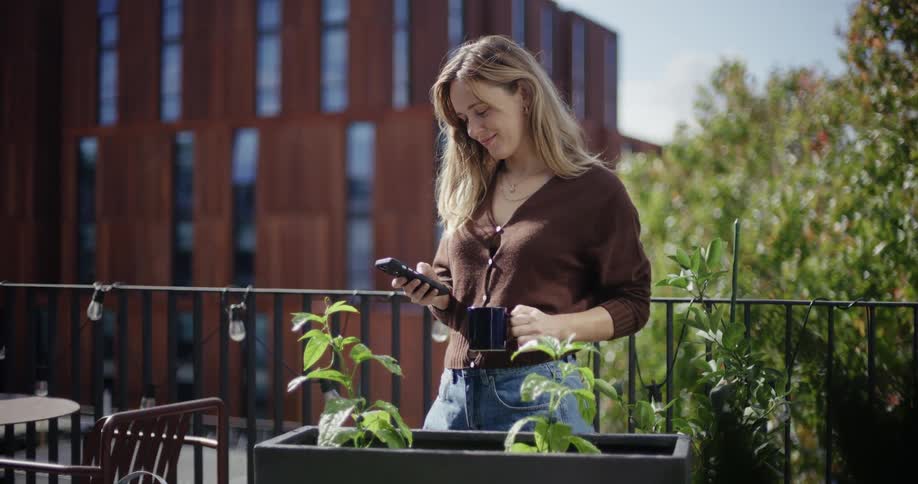Woman uses her phone while standing on a patio in the city