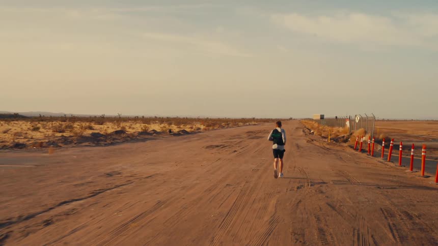 A person jogs alone on a dusty road through a desert landscape