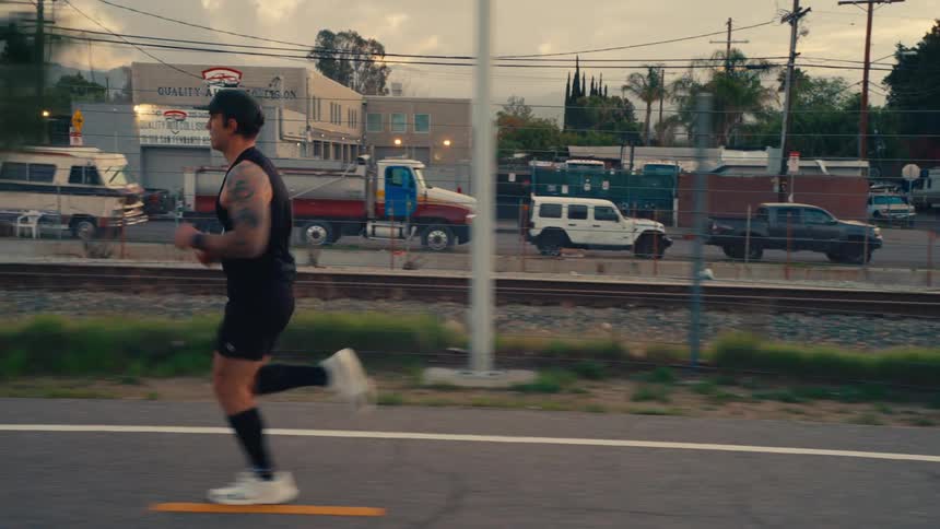 A man runs along a street beside railroad tracks in an urban industrial area