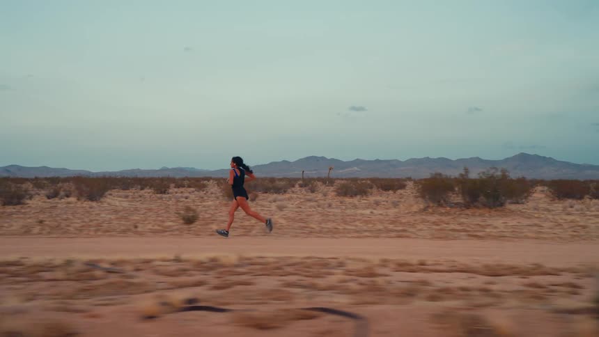A person runs alone on a desert path with mountains in the background