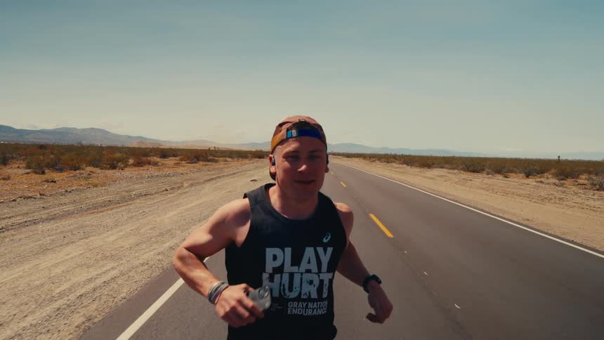 A man runs alone down a desert highway under the bright midday sun