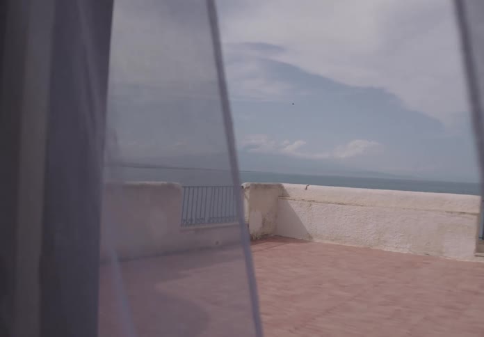 Sheer curtains swaying in the breeze reveal a mountain beyond a rooftop deck