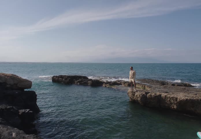 A man stands on a rock formation in the sea under a clear sky