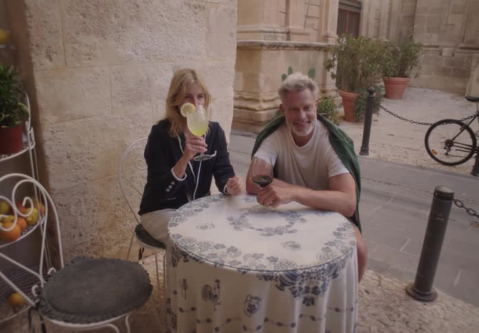 Man and woman have drinks while sitting at an outdoor table near the street