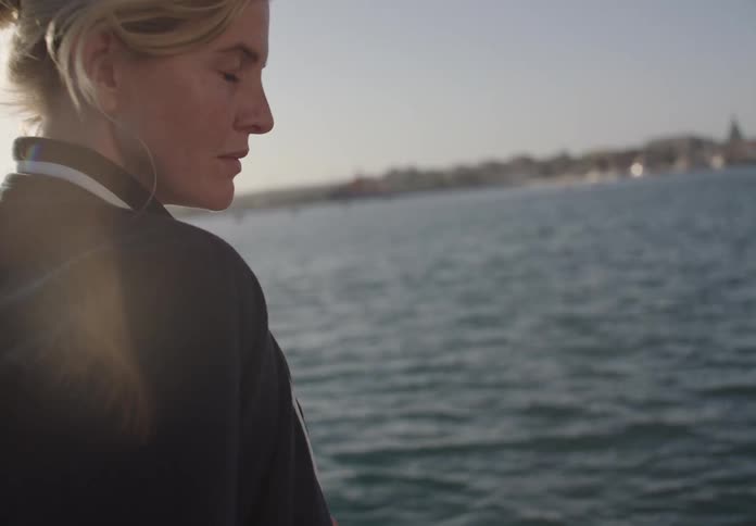A woman stands by the lake on a windy day