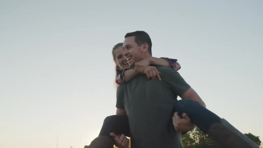 Man carrying a woman on his back spins while outdoors