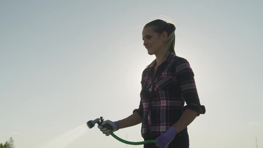 Woman outdoors and handling a hose with water jet