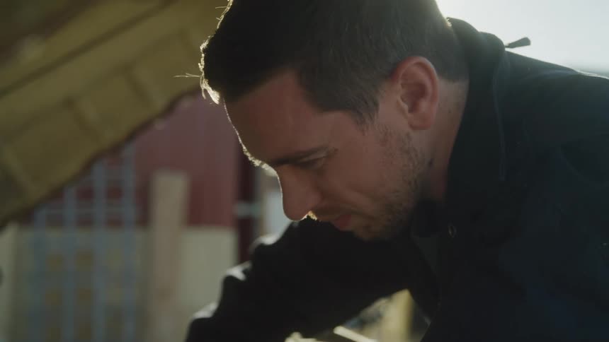 A man leans over a vehicle engine working intently under bright sunlight