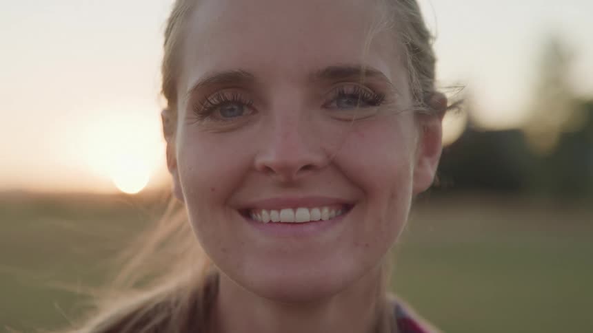 Close up portrait of a young woman smiling while standing outdoors at sunset