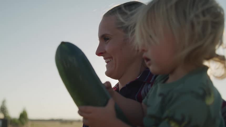 A woman is carrying her daughter who is holding a vegetable