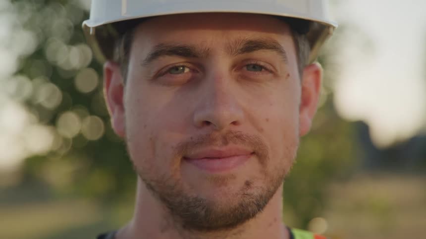 A man wearing a helmet and a green vest stands outdoors around midday