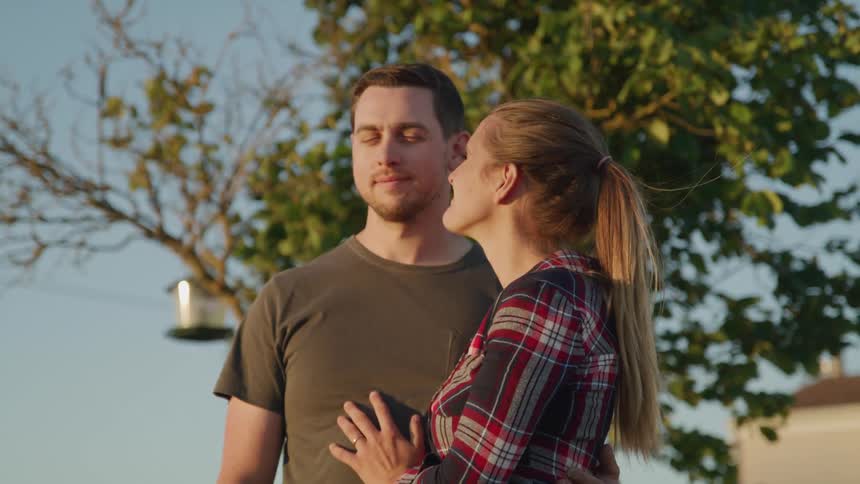 A couple stands close together outdoors gazing into each others eyes with affection
