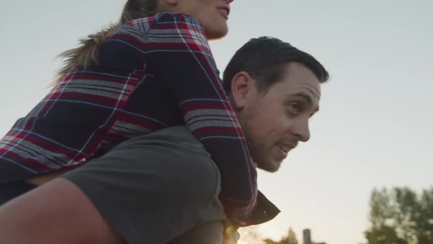 A man stands as his young wife jumps on his back both enjoying a good time outdoors around midday