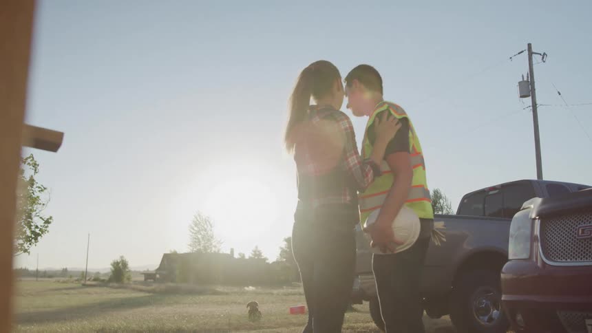 Young woman hugs and kisses her husband goodbye outdoors as he leaves for work in the morning
