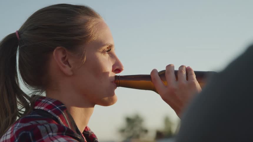 Woman in flannel drinking beer from a bottle outdoors